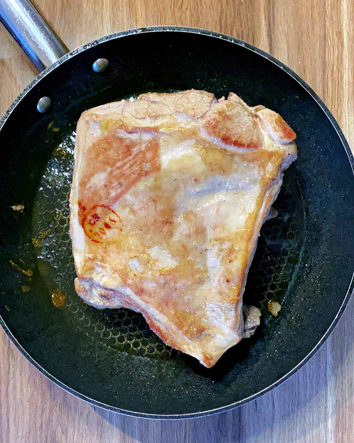 Browned lamb shoulder in a frying pan.