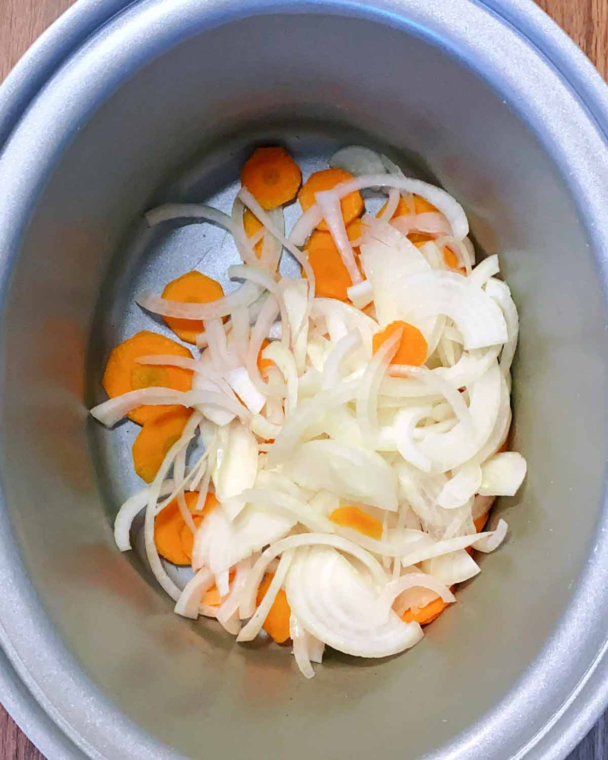 Chopped onion and carrot in a slow cooker bowl.