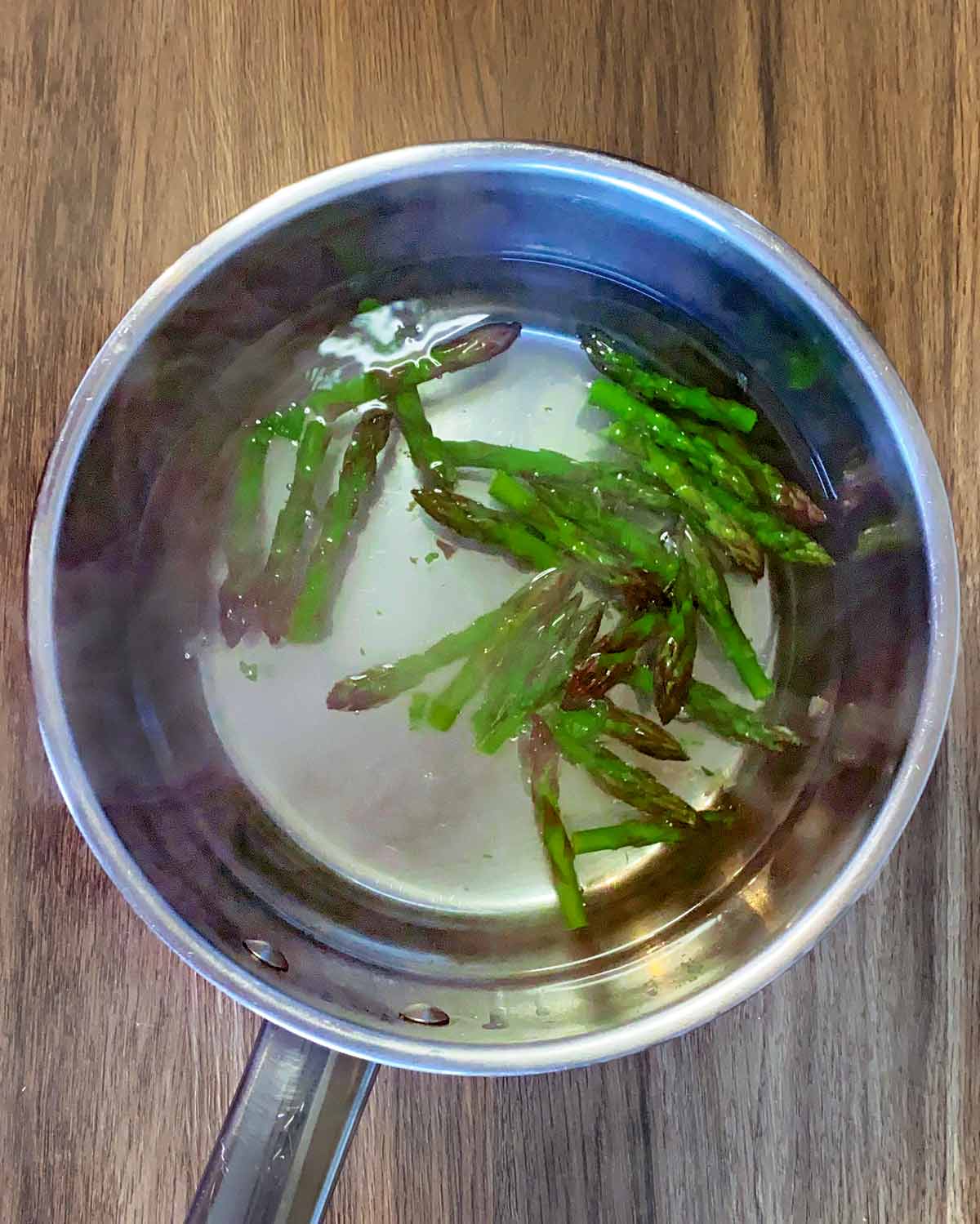 Asparagus tips being cooked in a pan.