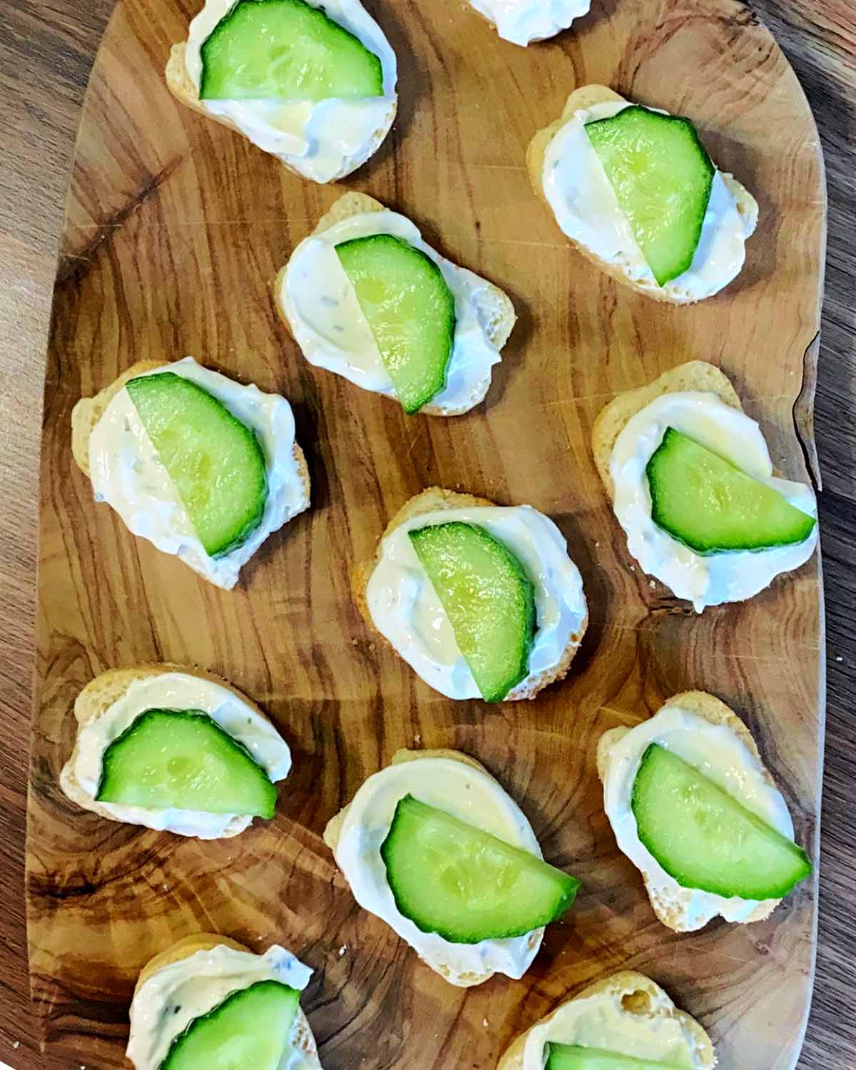 Crostini topped with cream cheese and half a slice of cucumber.