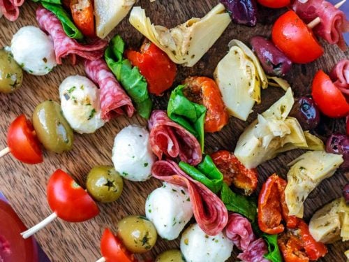 A row of antipasto skewers on a wooden board.