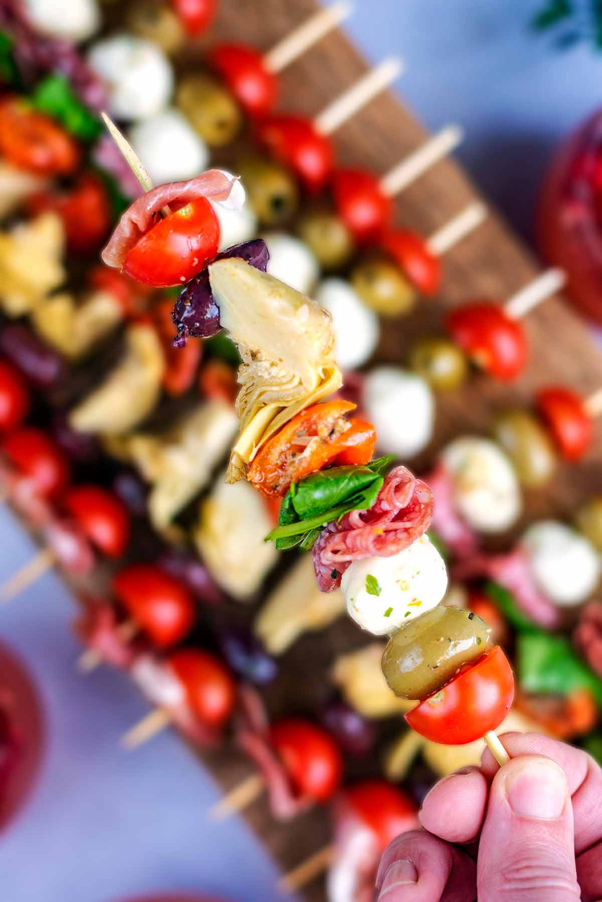 A hand holding an antipasto skewer over a board of more skewers.