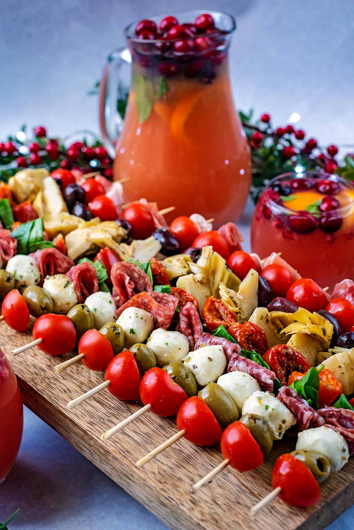 A serving board full of antipasto skewers in front of a jug of punch.