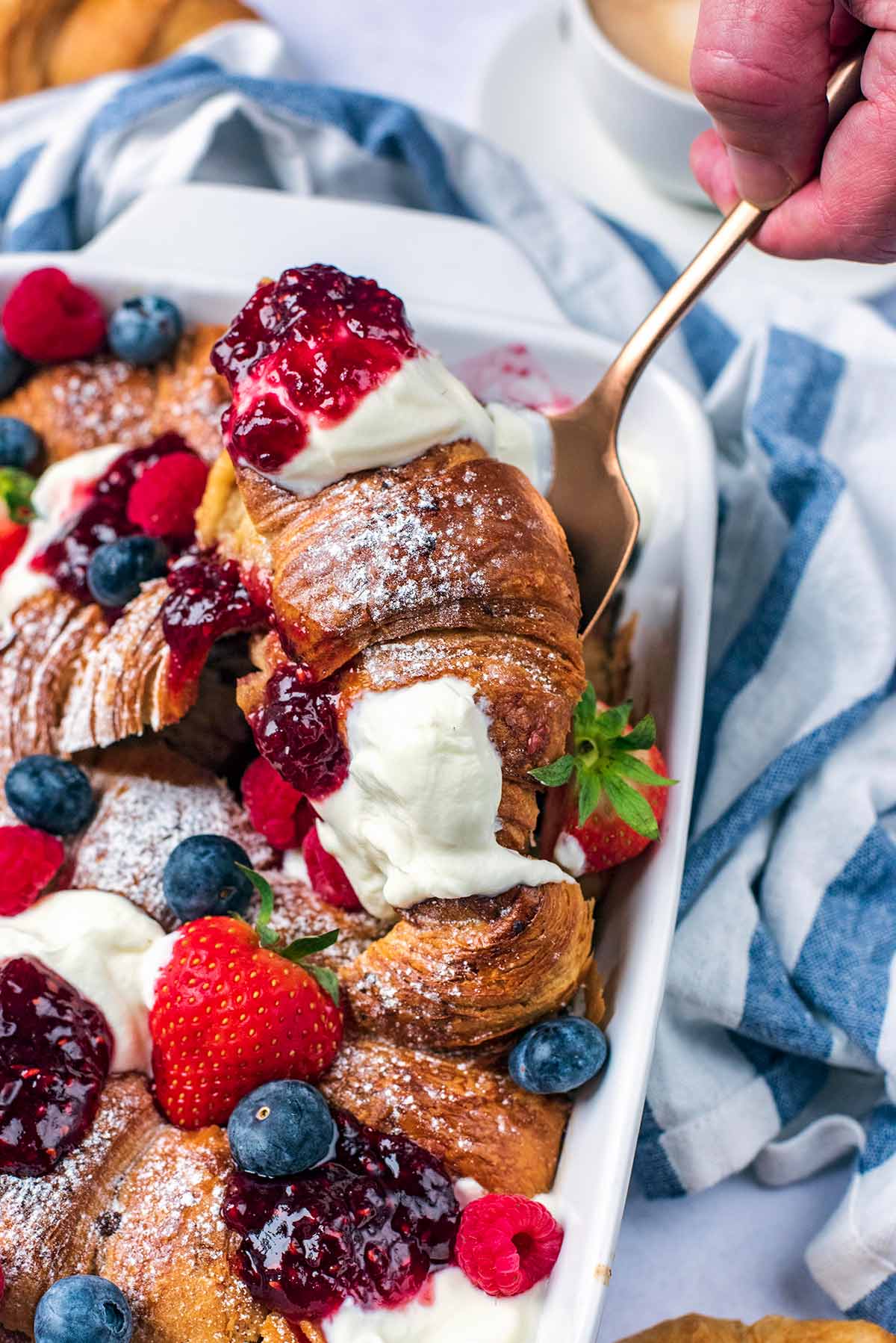 A spoon lifting out some baked croissant from a baking dish.