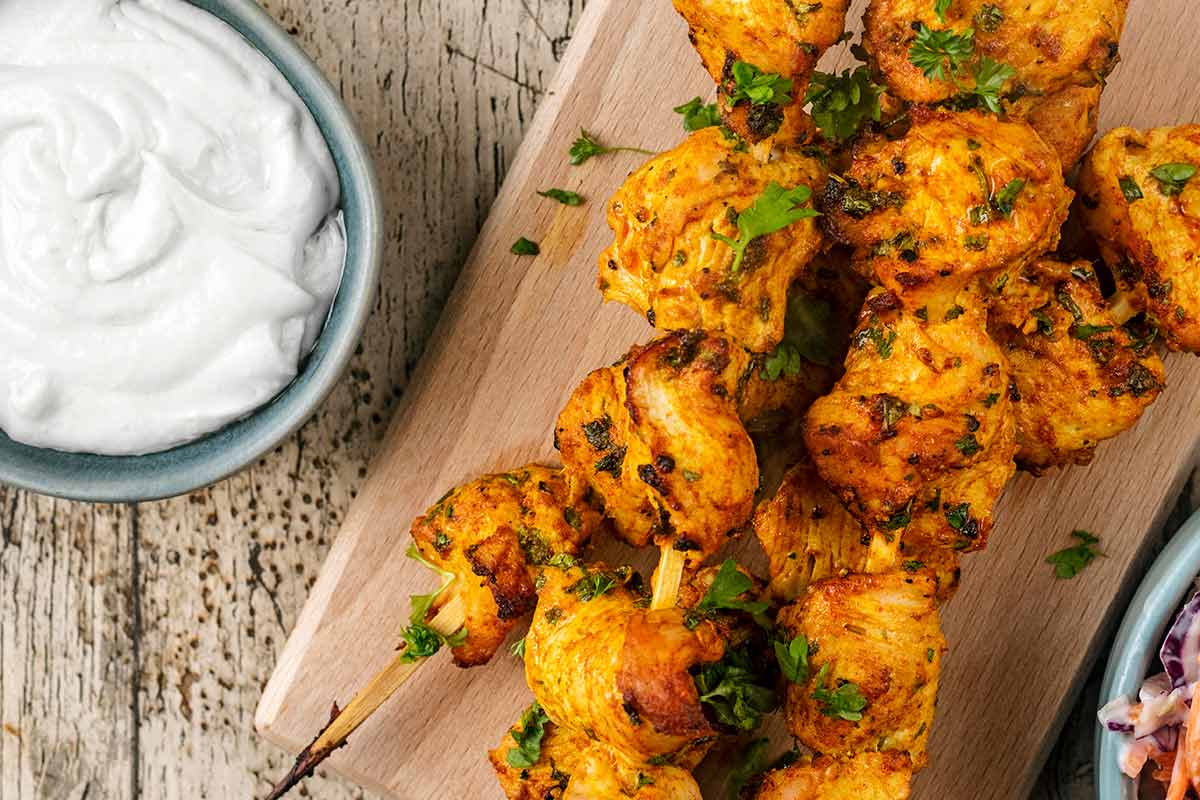 Shish kebabs on a board next to a bowl of white sauce.