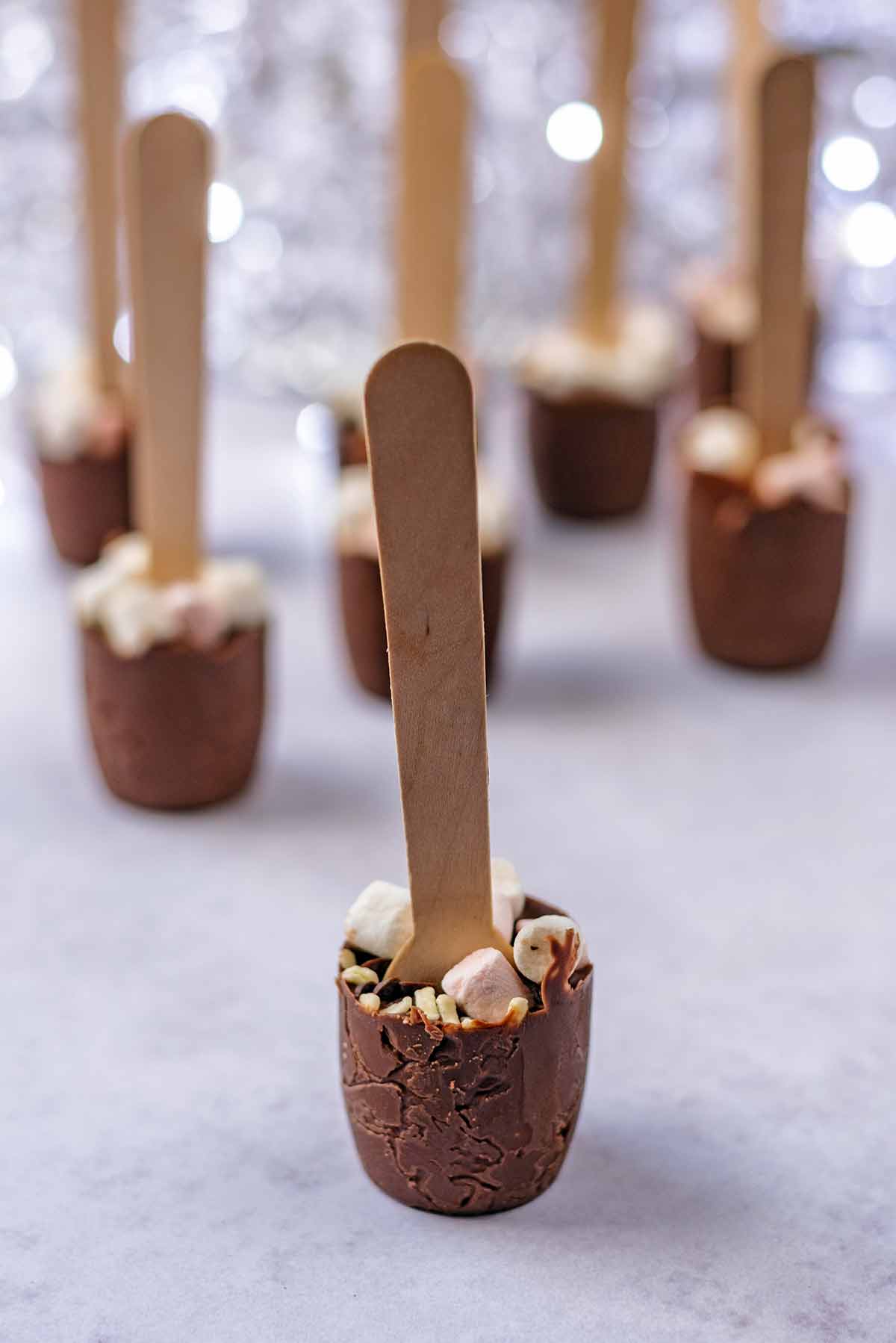 Eight hot chocolate spoons stood in front of a sparkly background.