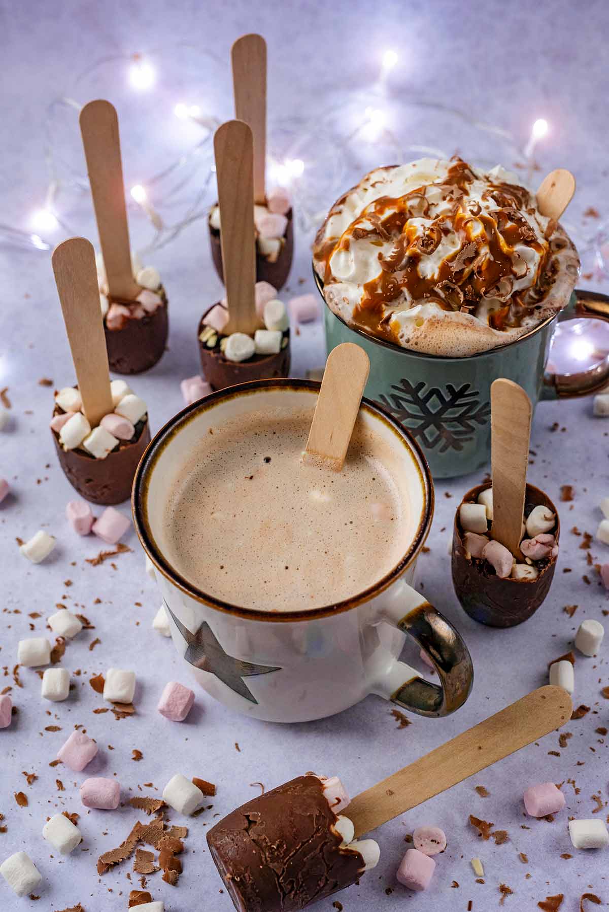 Mugs of hot chocolate surrounded by chocolate spoons and fairy lights.