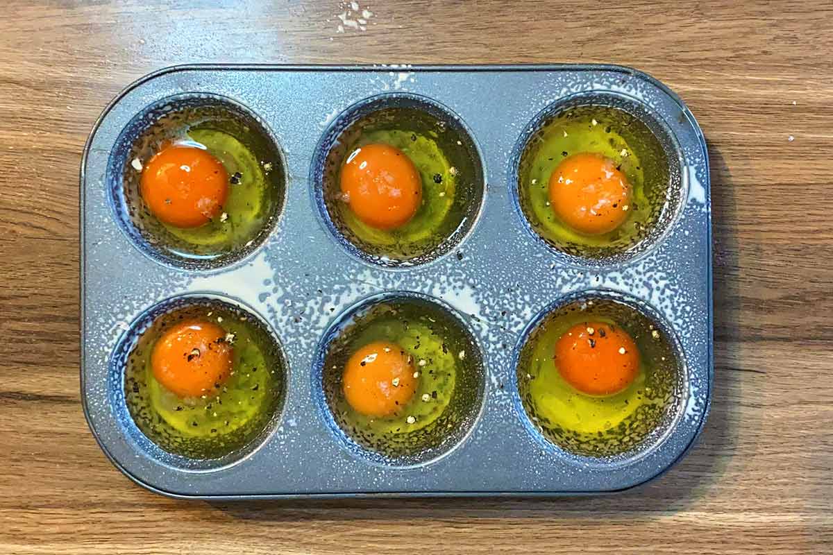 A six hole muffin tin containing cracked eggs.