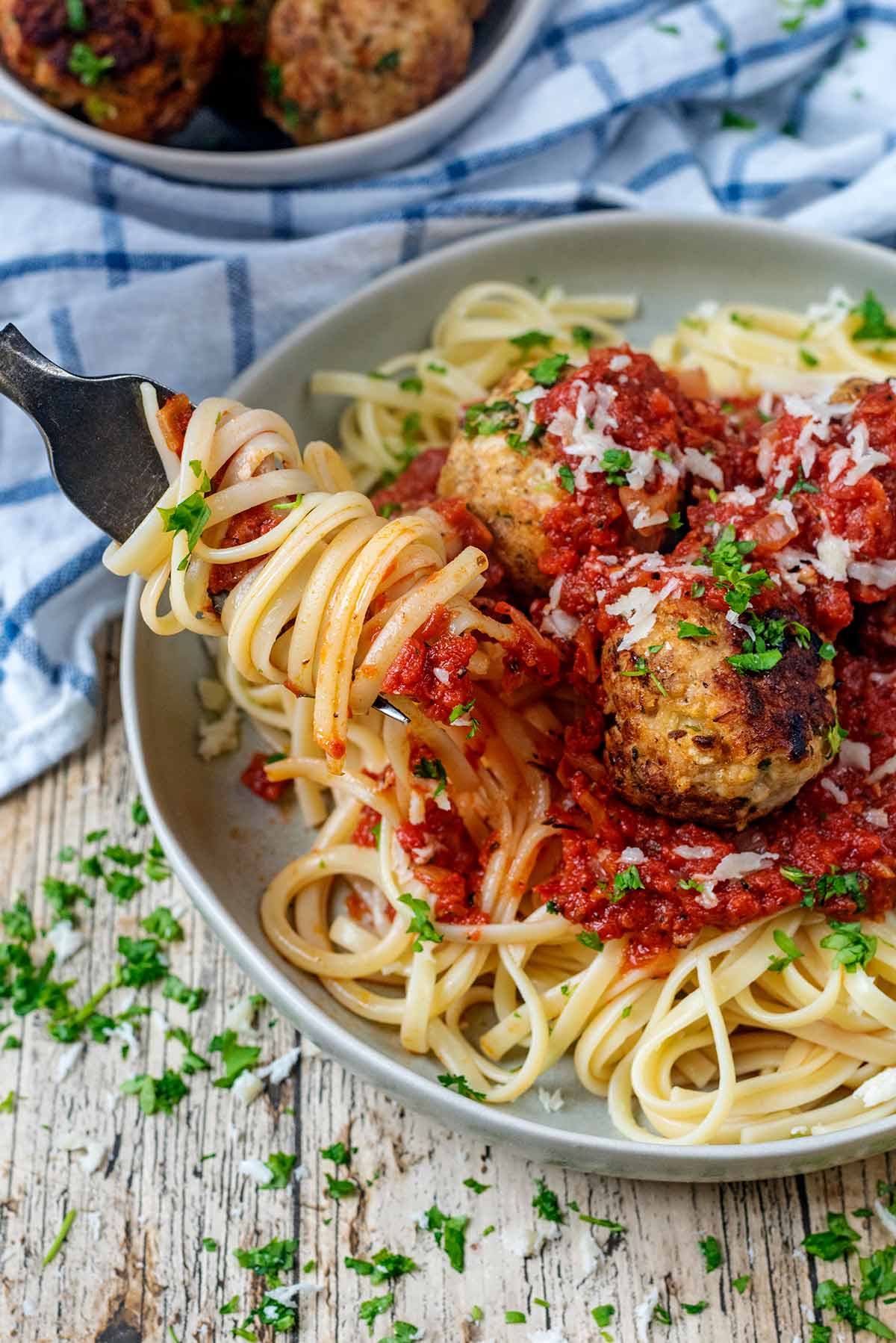 A fork picking up some spaghetti from a plate with meatballs on it.
