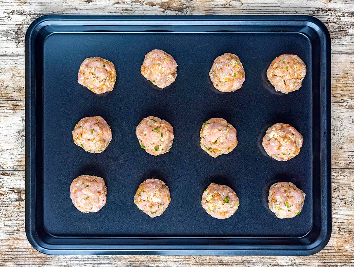Twelve uncooked meatballs on a baking tray.