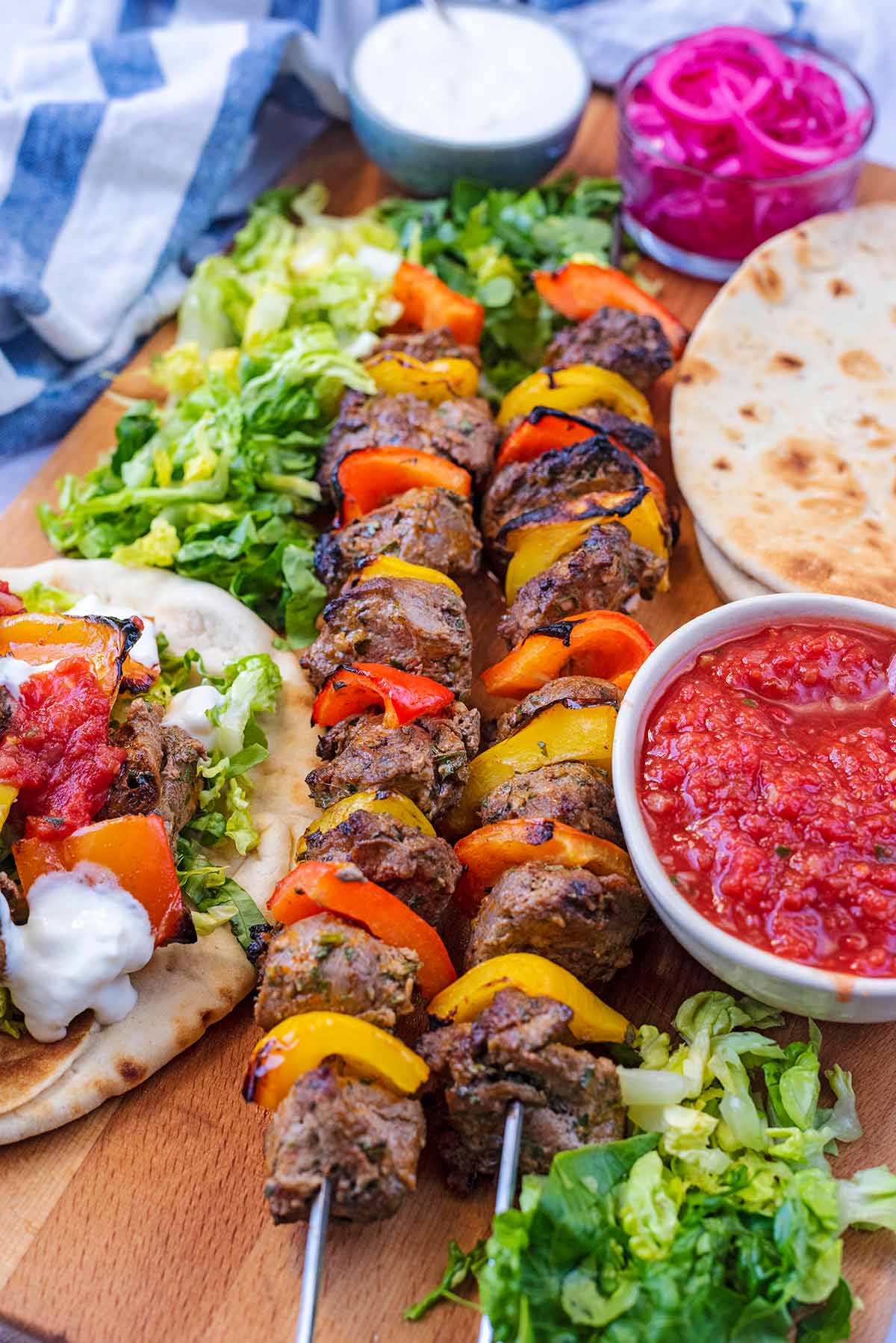 Shish kebabs on a board with flat breads and chilli sauce.