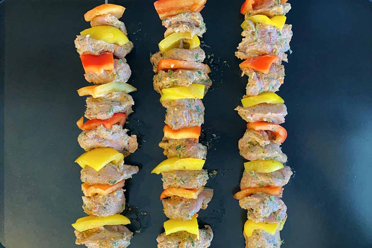 Three lamb shish kebabs on a black baking tray.