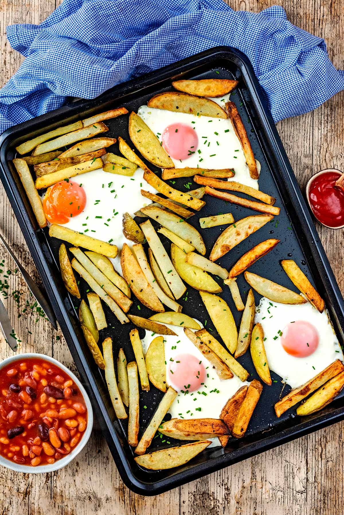 A baking tray with chips and cooked eggs on it.