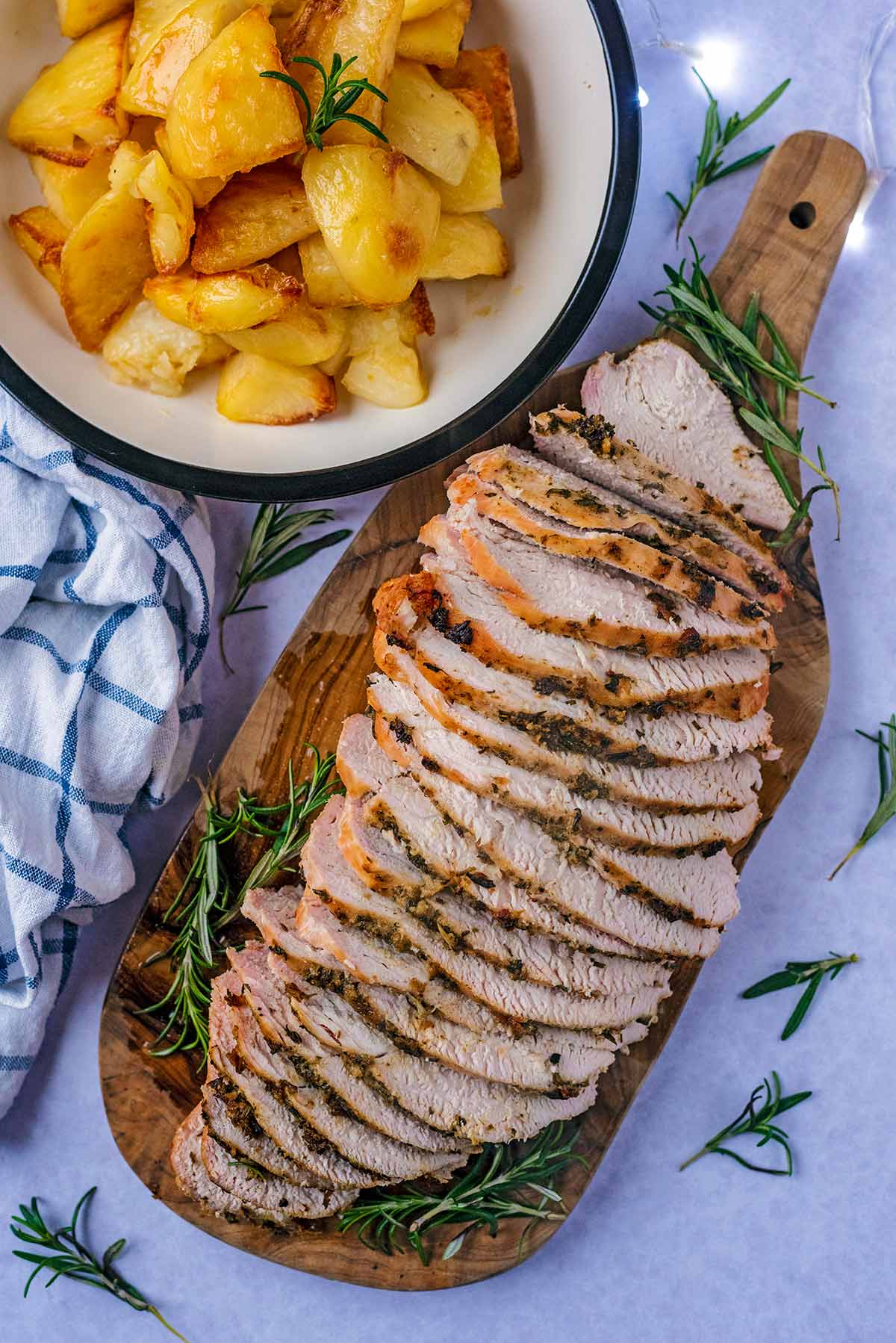 Sliced roast turkey on a serving board next to a bowl of roast potatoes.