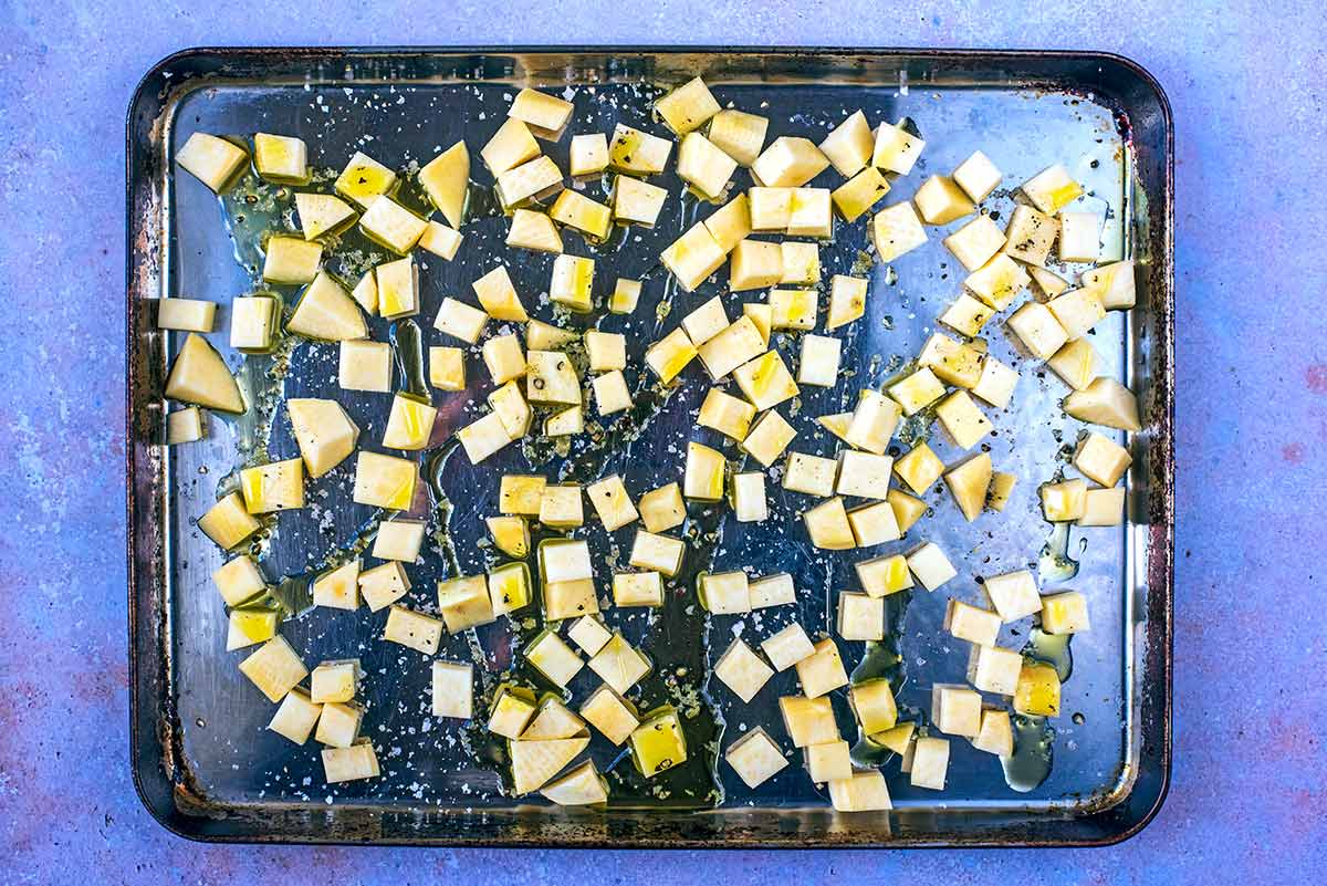 Small cubes of raw swede on a baking tray with oil drizzled over.