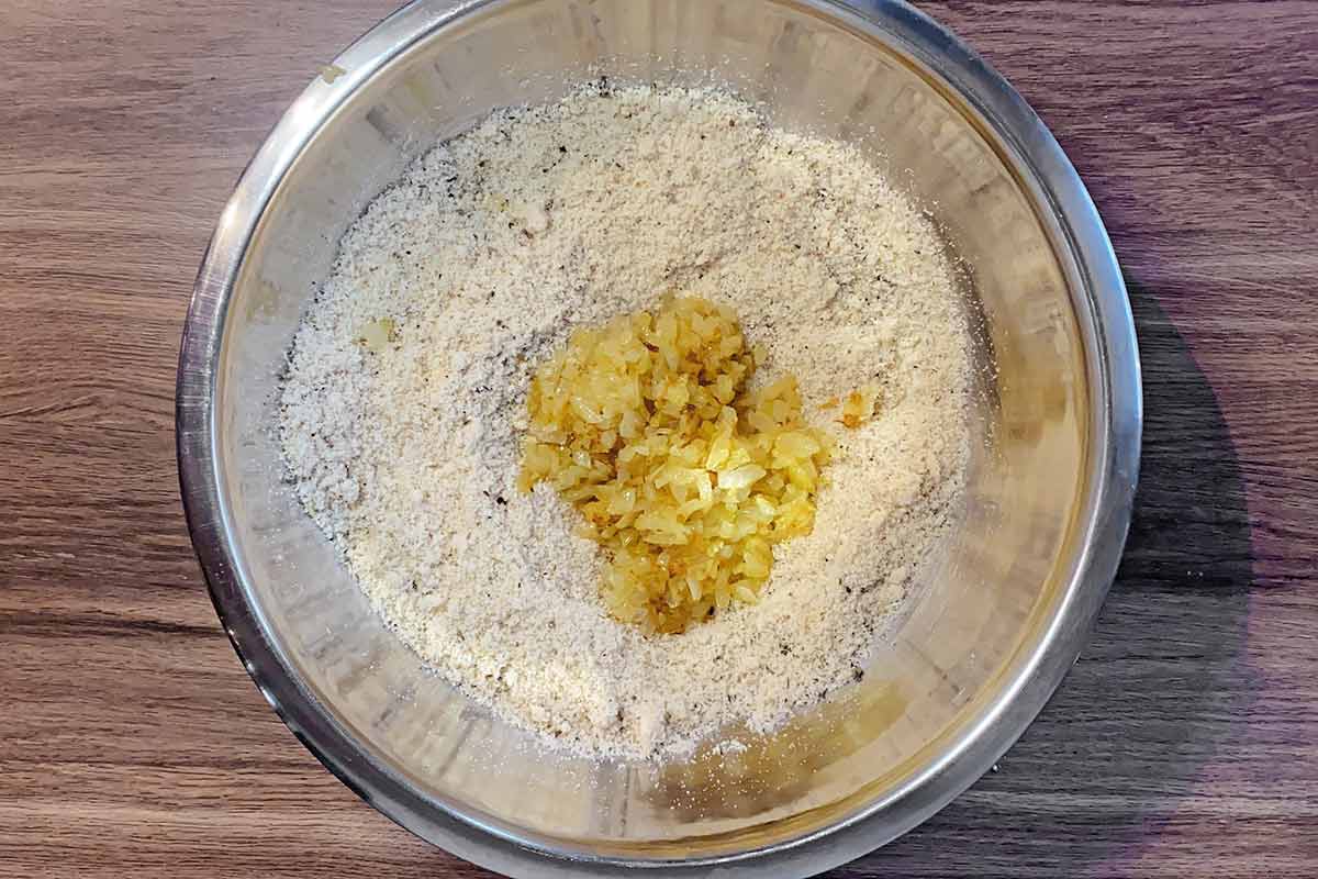 Cooked onions added to a bowl of seasoned breadcrumbs.