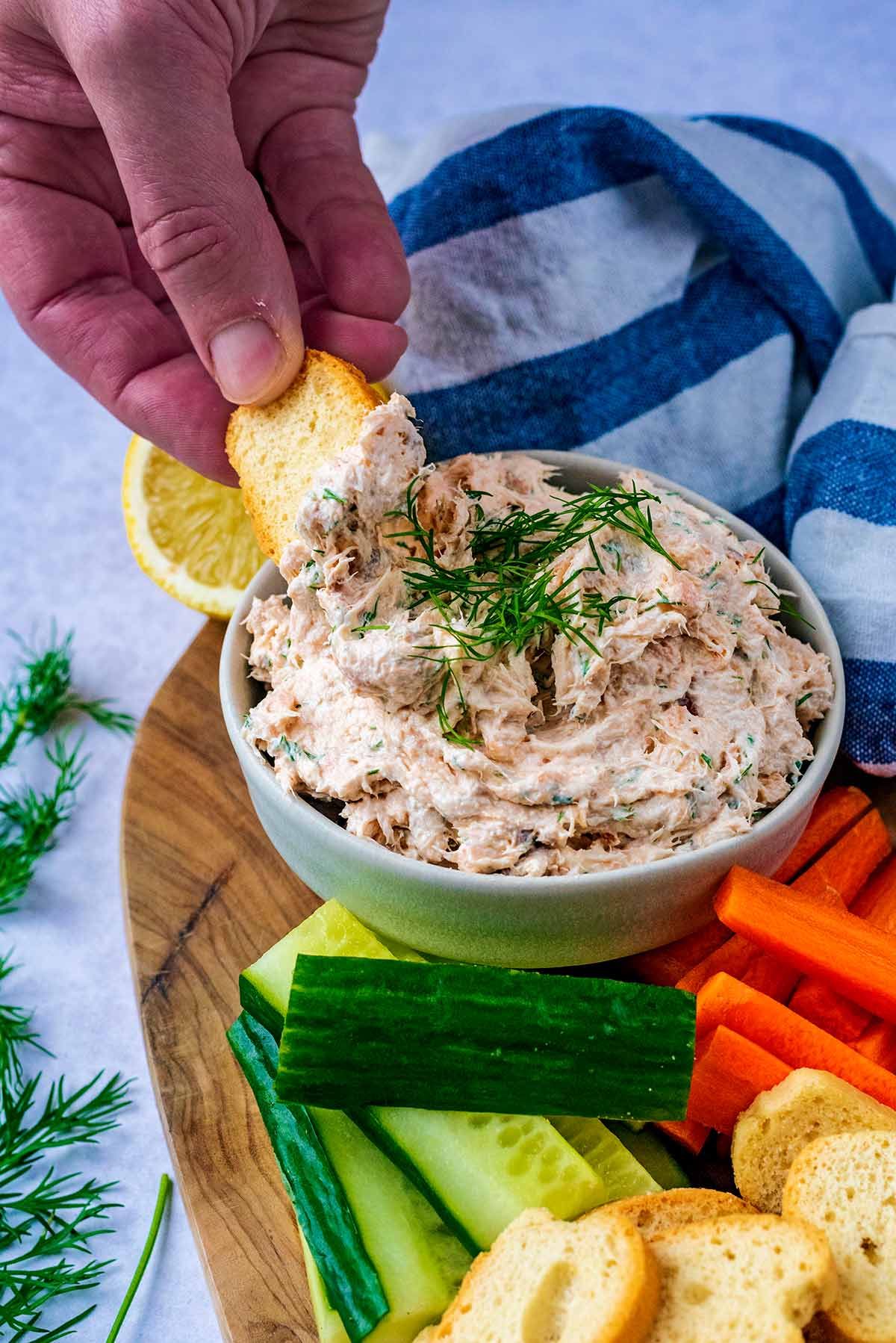 A crostino being dipped into a bowl of salmon pate.