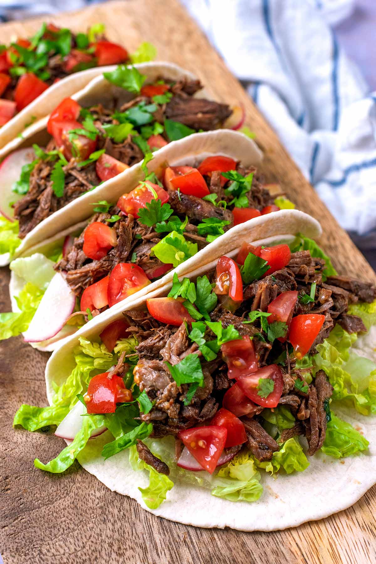 A row of shredded beef tacos on a wooden serving board.