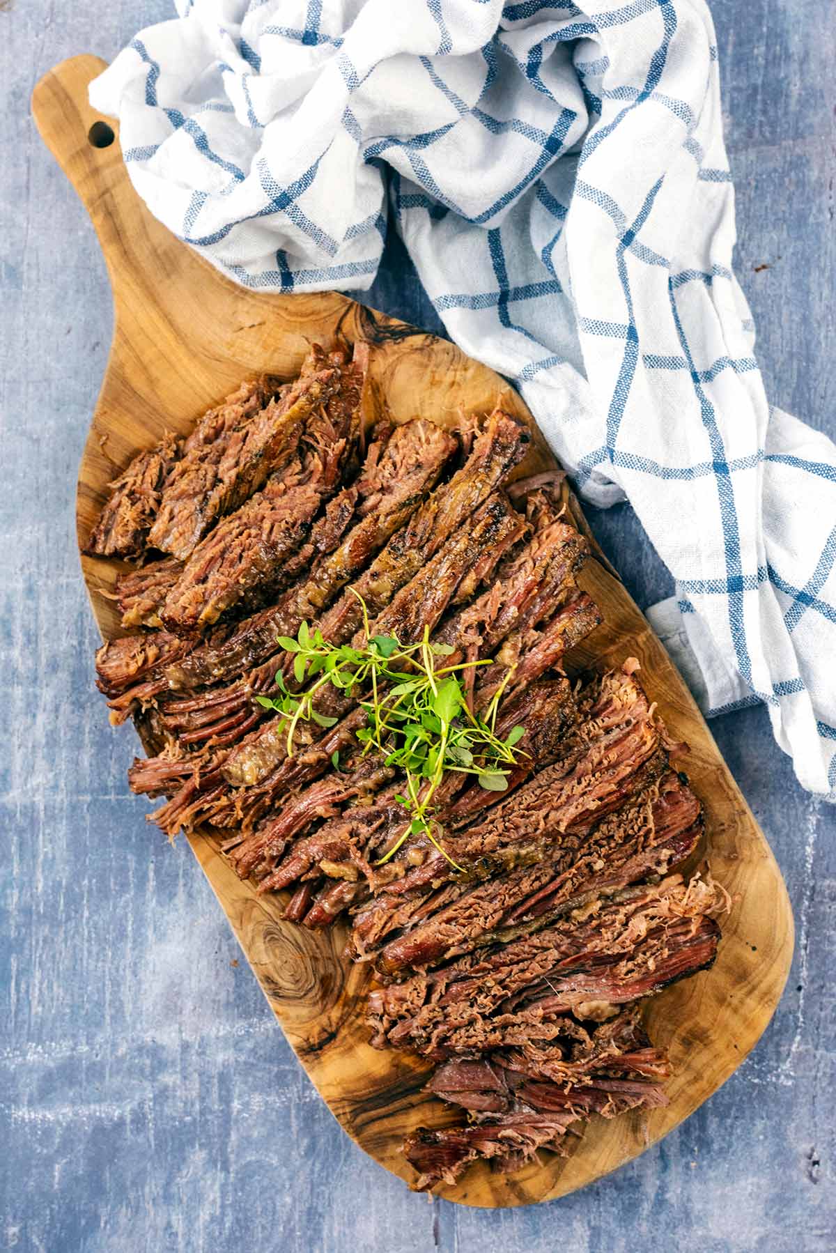 A wooden serving board with slices of cooked beef on it.