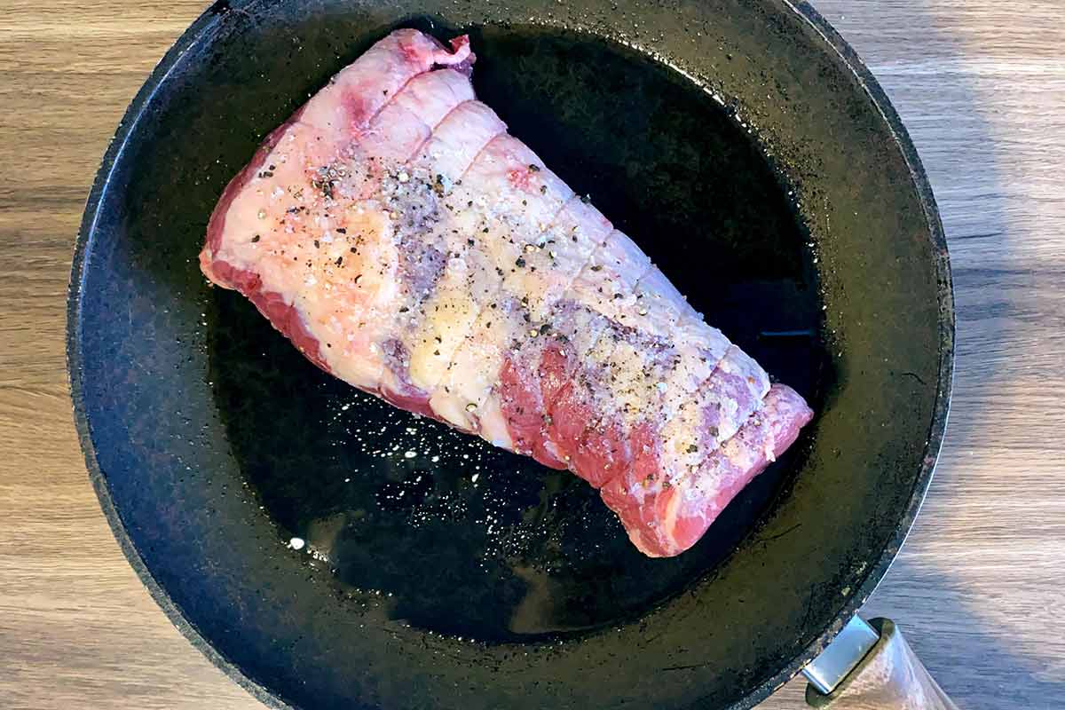 A joint of beef browning in a frying pan.