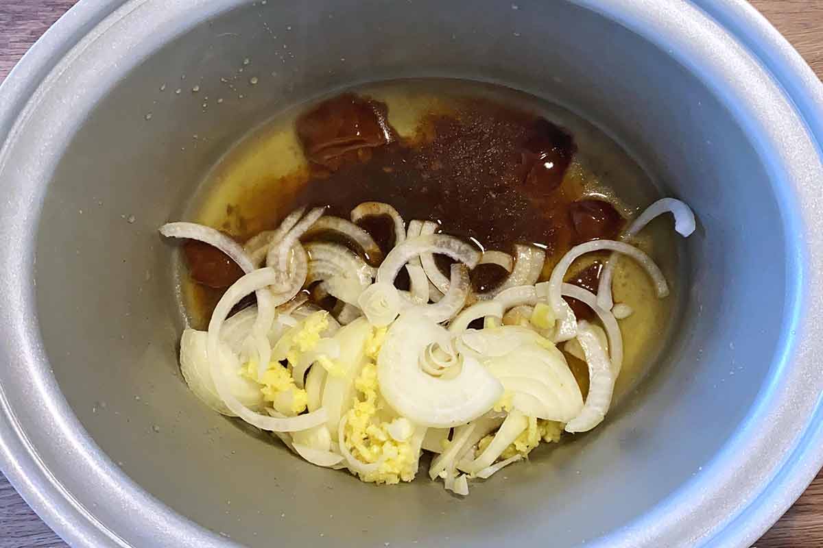 Stock, sliced onions, garlic and thyme in a slow cooker bowl.