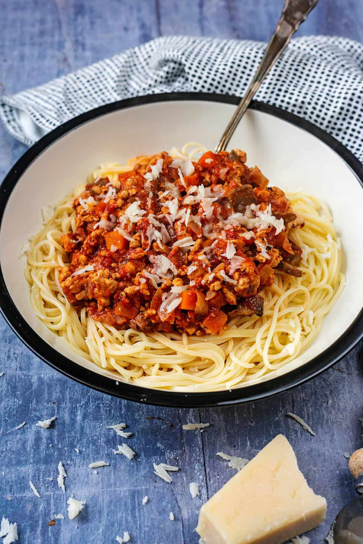 A bowl of turkey bolognese with a block of Parmesan cheese in front of it.