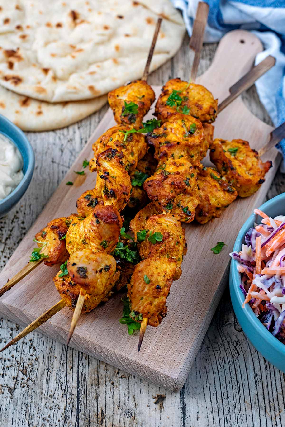 A wooden serving board with four turkey skewers on it.