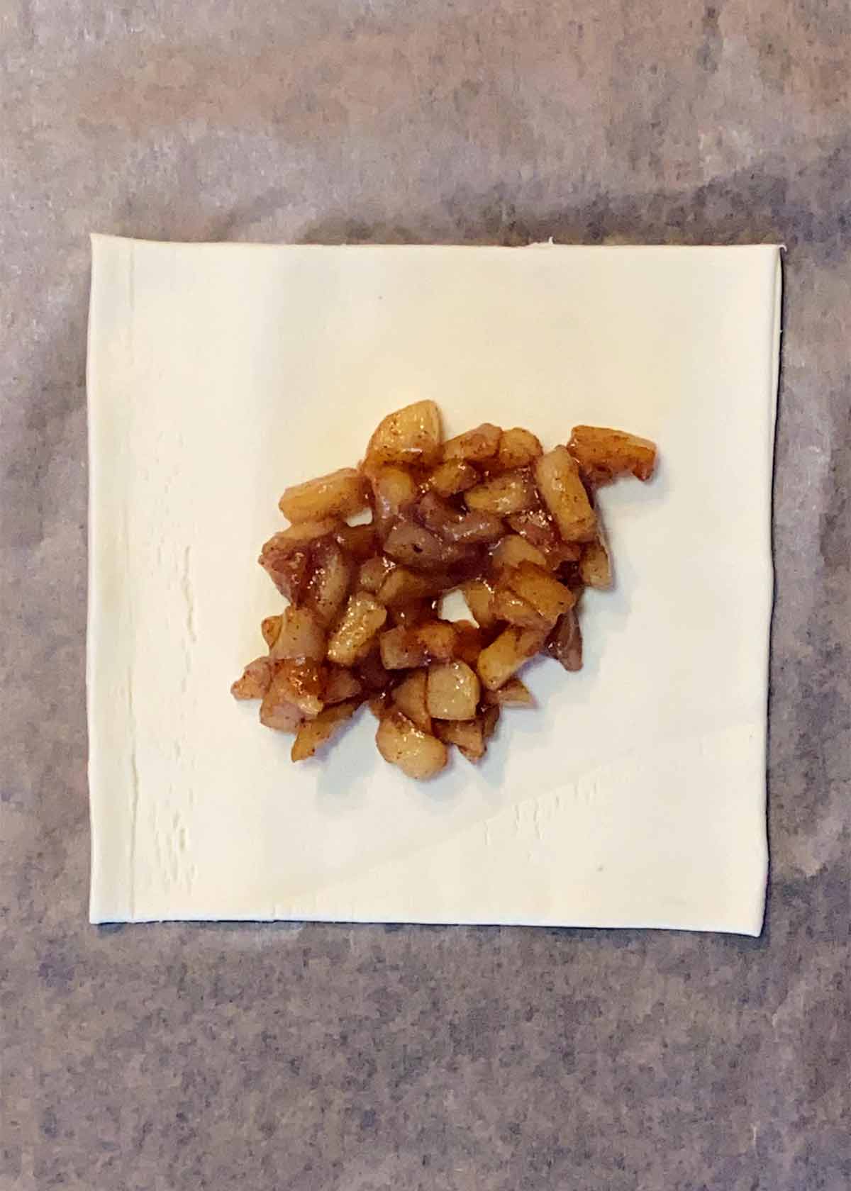 A square of pastry with some of the cooked apples in the middle.
