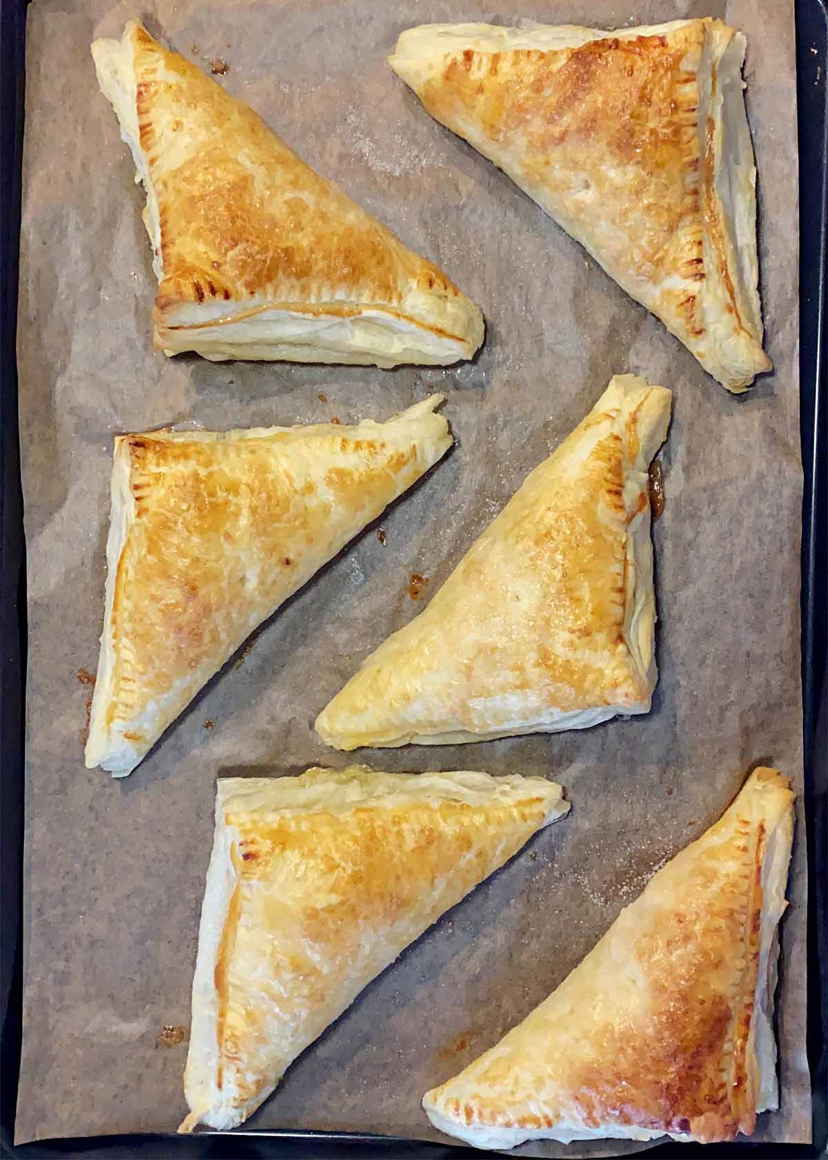 Six cooked turnovers on a baking tray.