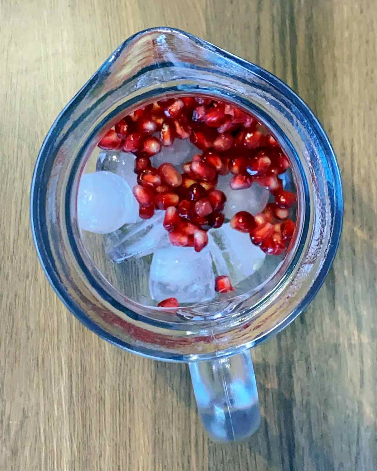 A large glass jug with ice and pomegranate seeds in it.