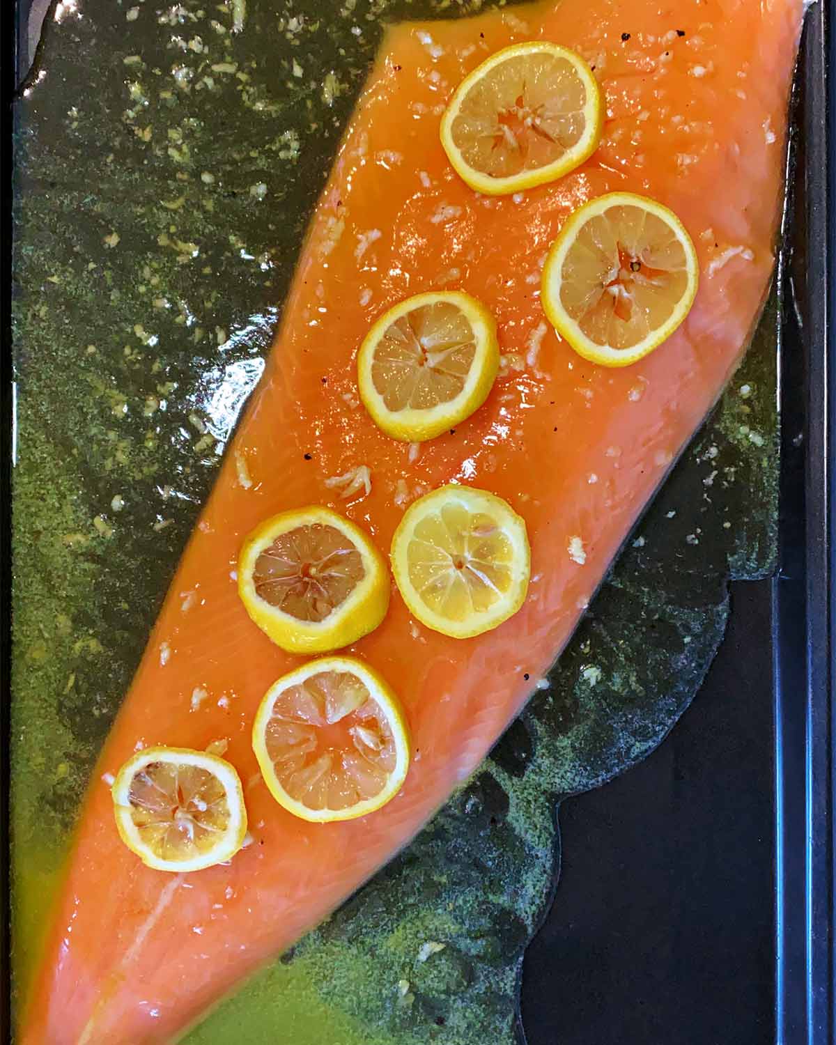 A side of salmon on a baking tray covered in marinade and lemon slices.