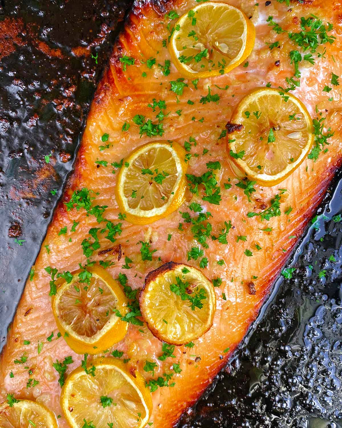 A cooked side of salmon with chopped herbs on top.