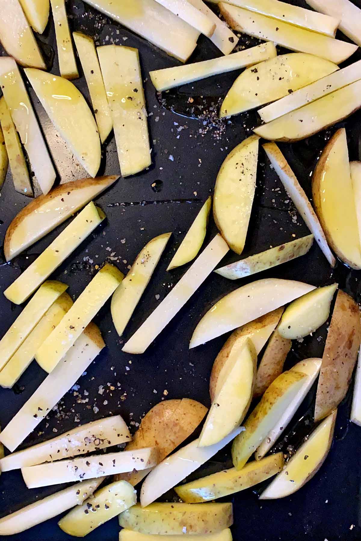 Seasoned, uncooked potato chips on a large baking tray.