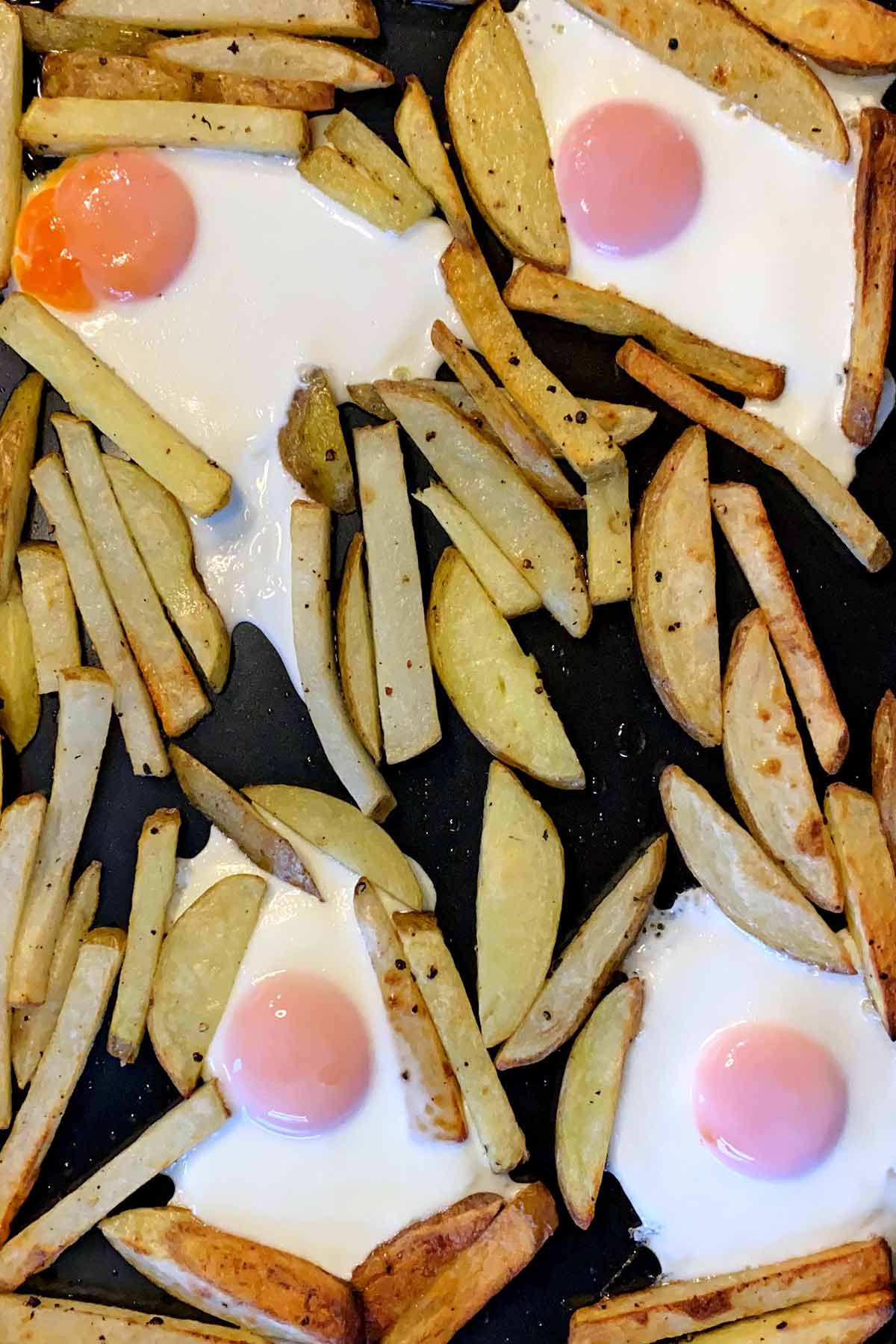 Cooked eggs amongst the cooked chips on a baking tray.