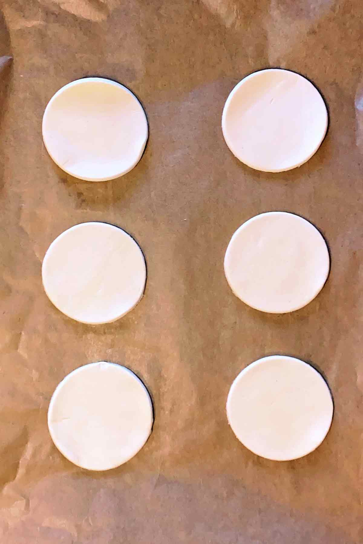 Six pastry disks on a lined baking tray.