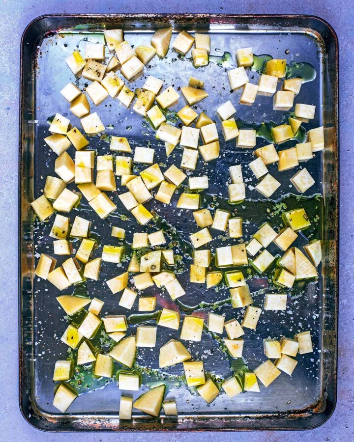 Small cubes of raw swede on a baking tray with oil drizzled over.
