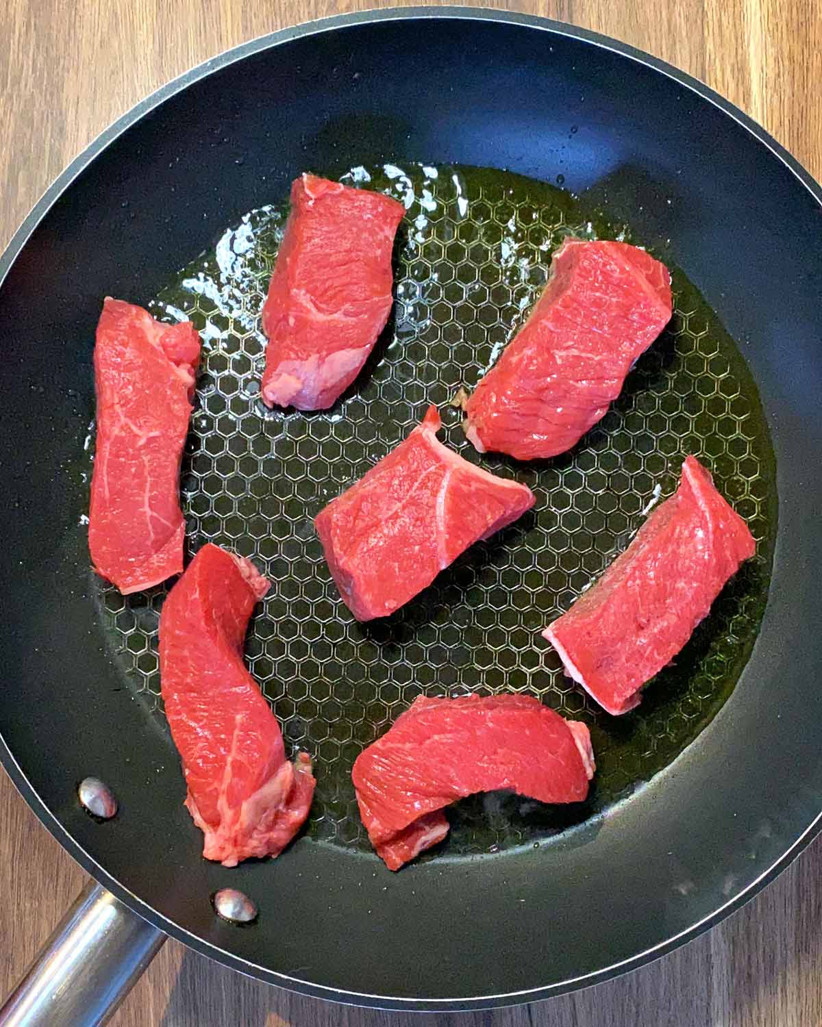 Large chunks of beef browning in a frying pan.