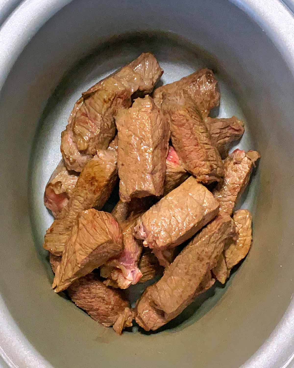 Chunks of browned beef in a slow cooker bowl.