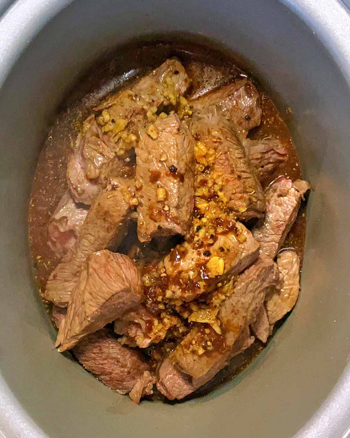 Browned beef and barbacoa marinade in a slow cooker bowl.