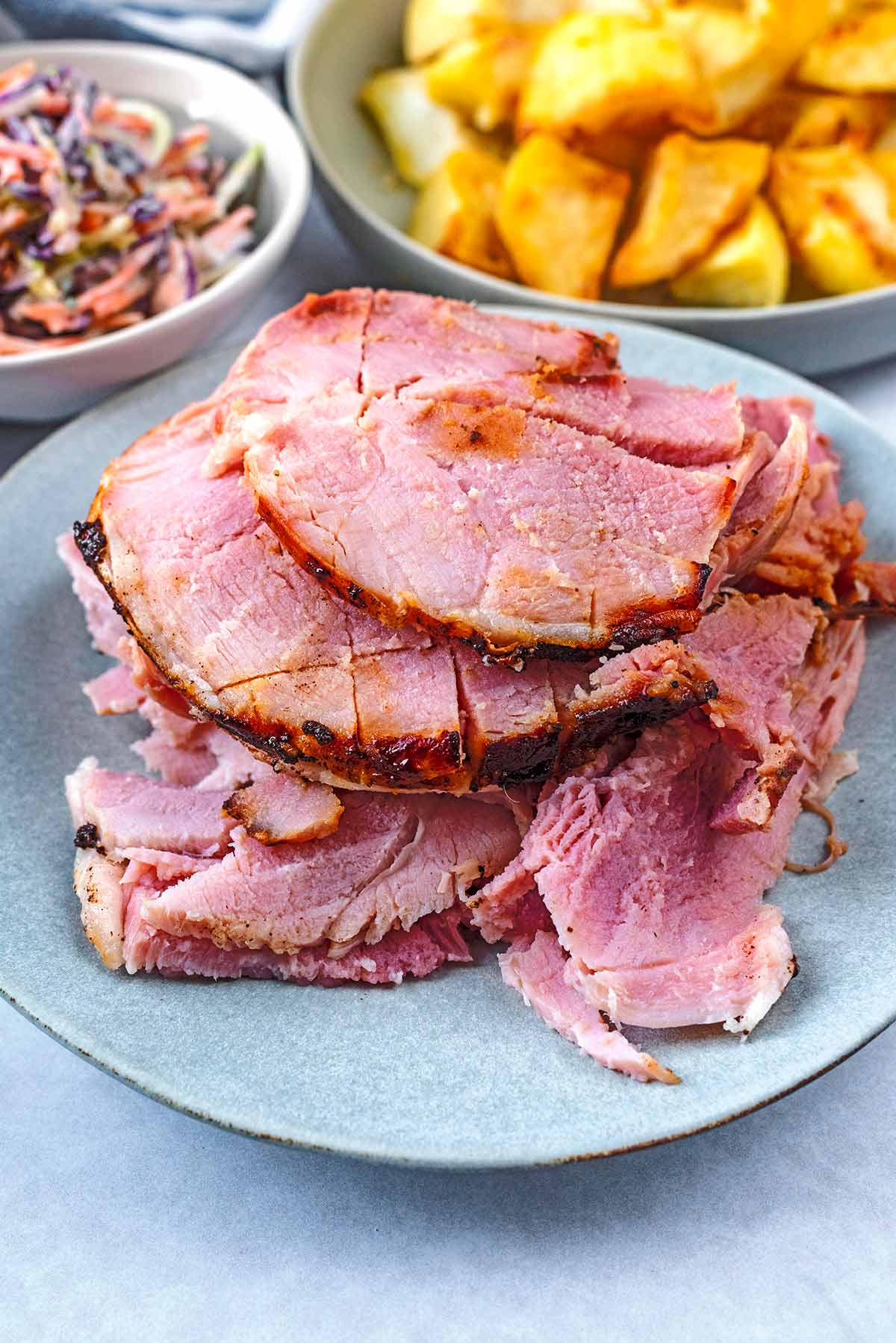 Slices of cooked ham in front of some roast potatoes.