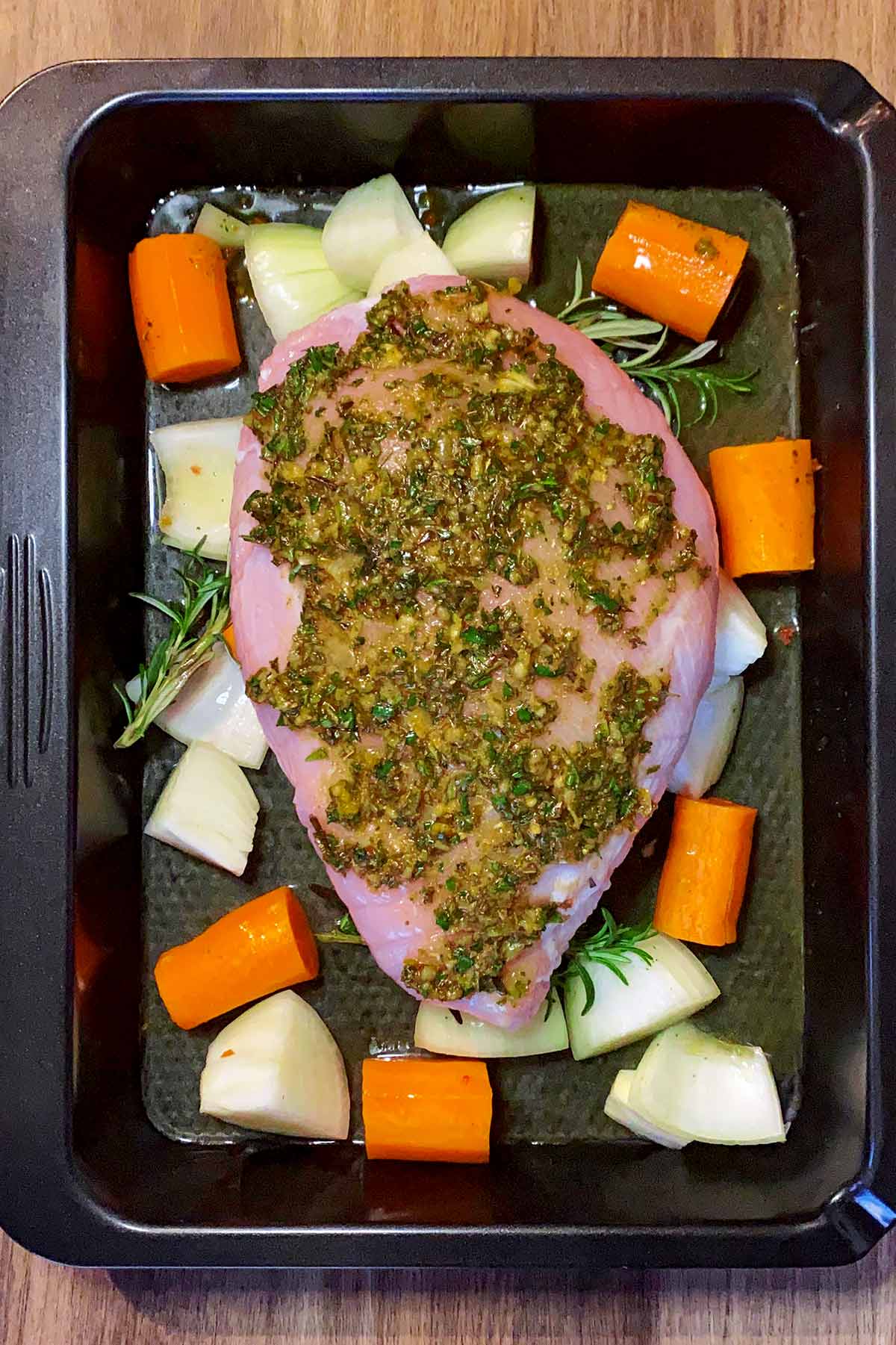 The smothered turkey breast on top of the vegetables with stock added to the tin.