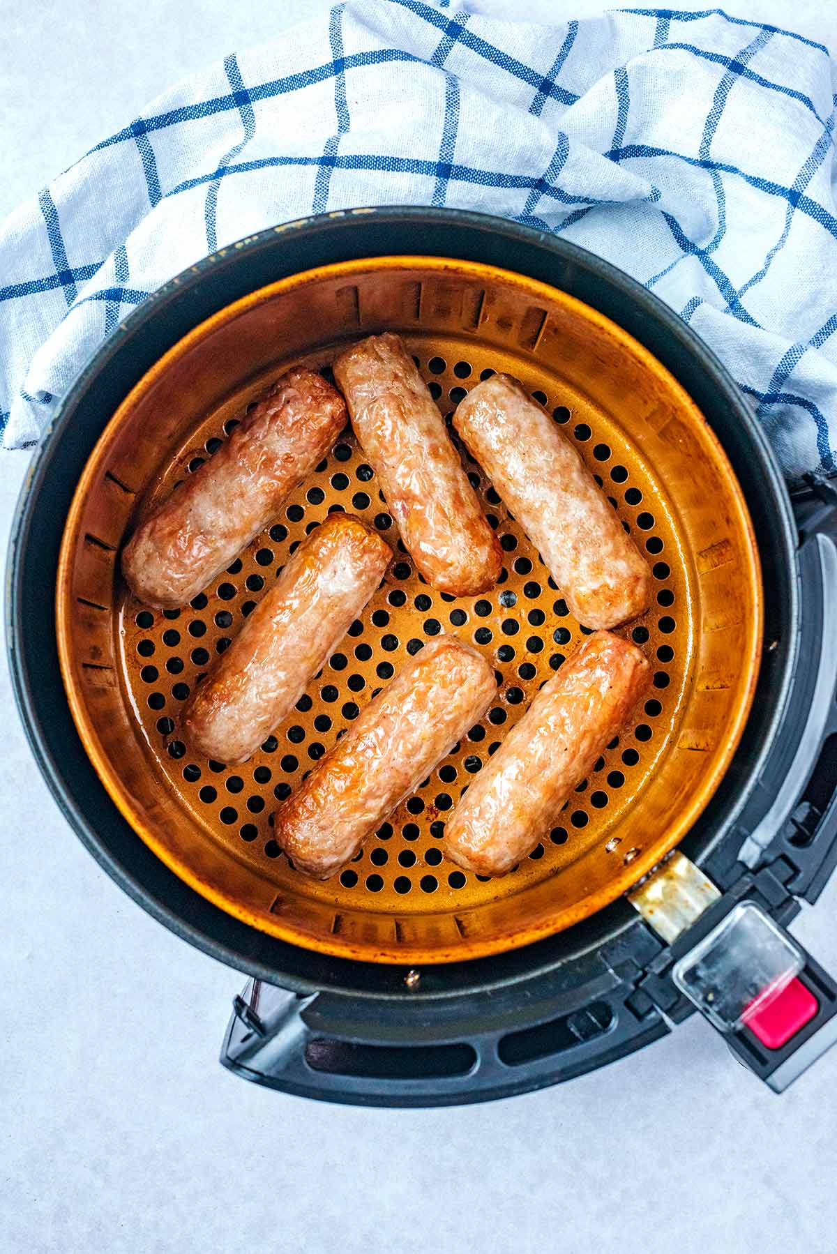 An air fryer basket containing cooked sausages.