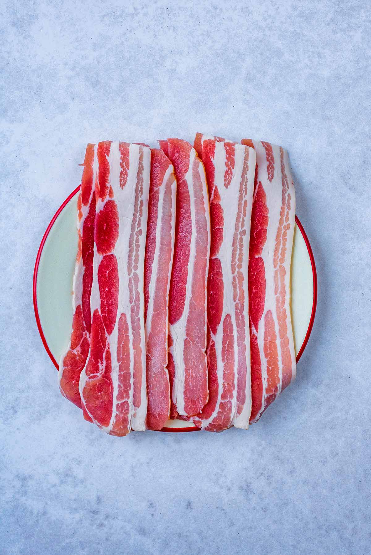 A plate with uncooked rashers of bacon on it.