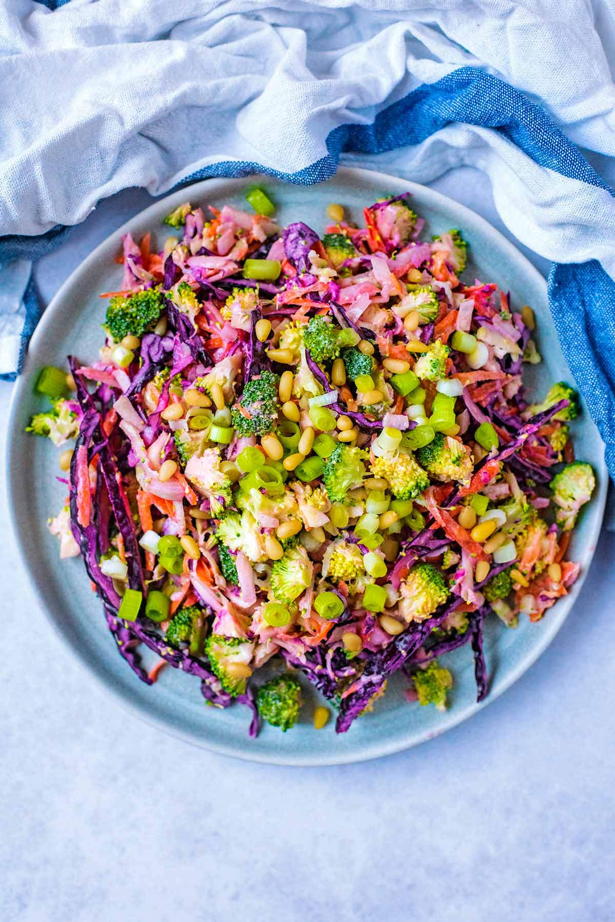 A large bowl of slaw containing broccoli, cabbage, onion carrot and pine nuts.