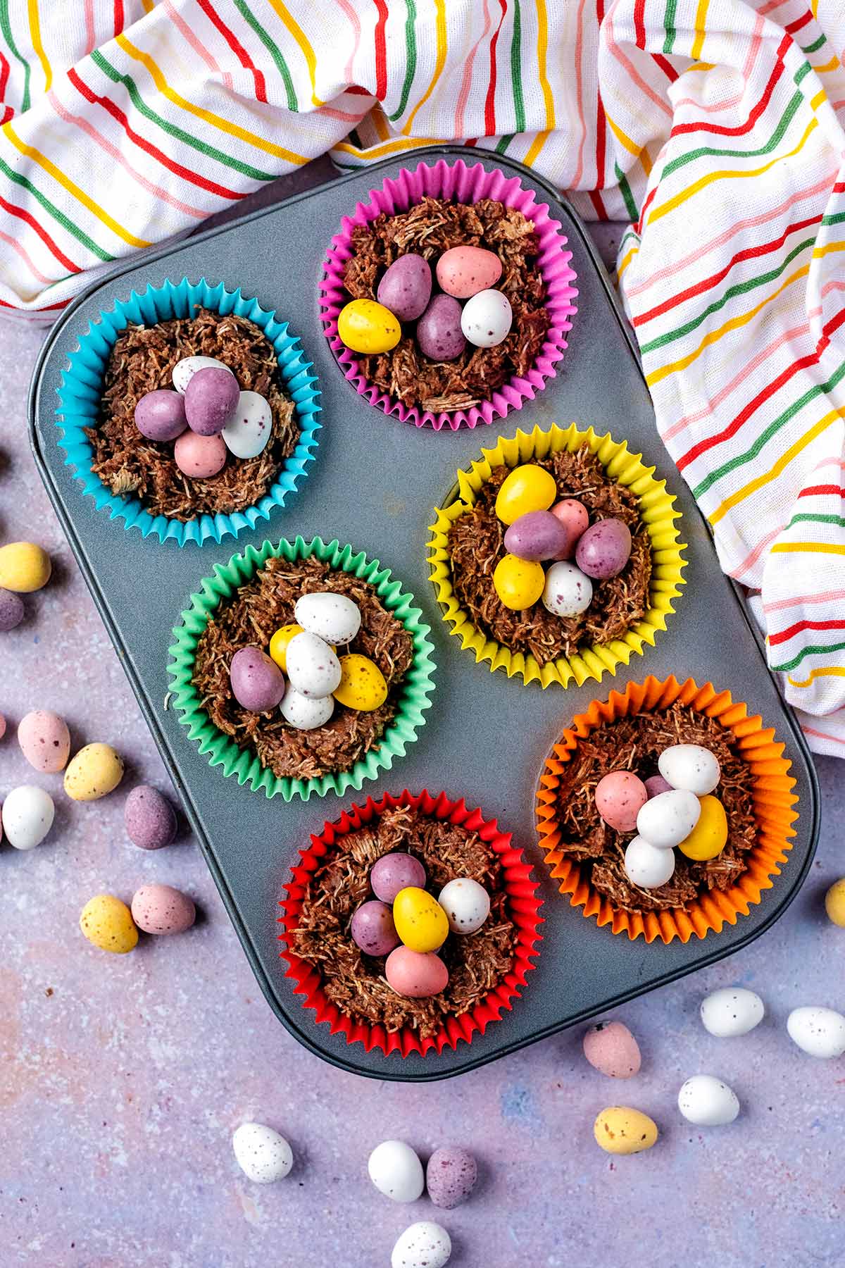 A six hold muffin tin with chocolate nests and mini eggs in them.