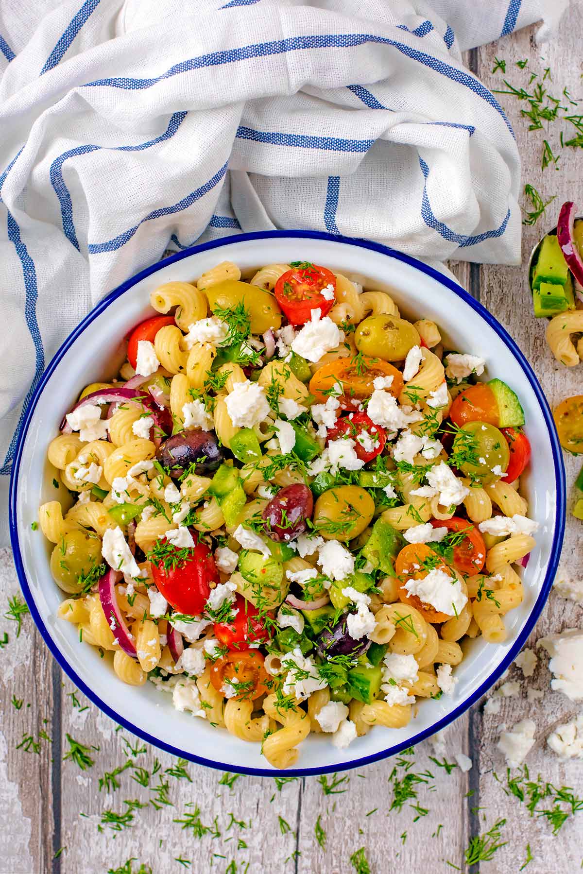 A bowl of pasta salad next to a blue and white towel.