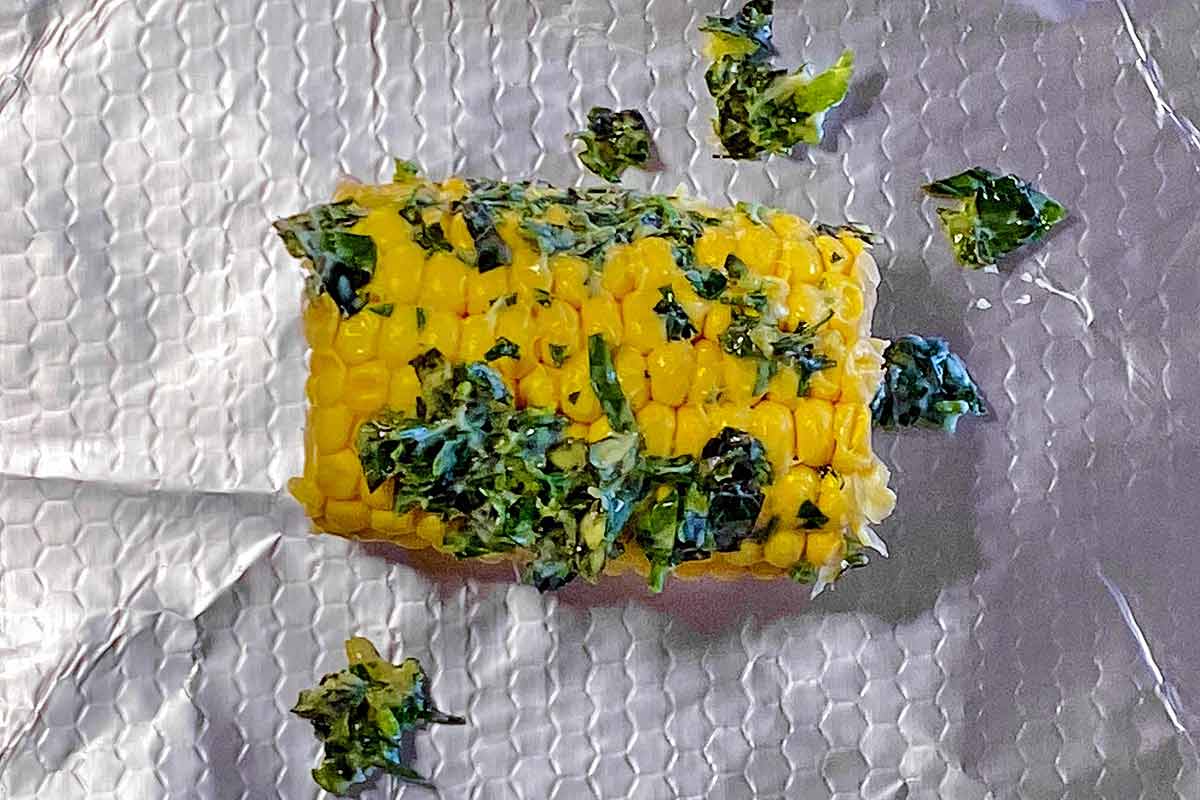 An ear of corn smothered in herb butter sat on some aluminium foil.