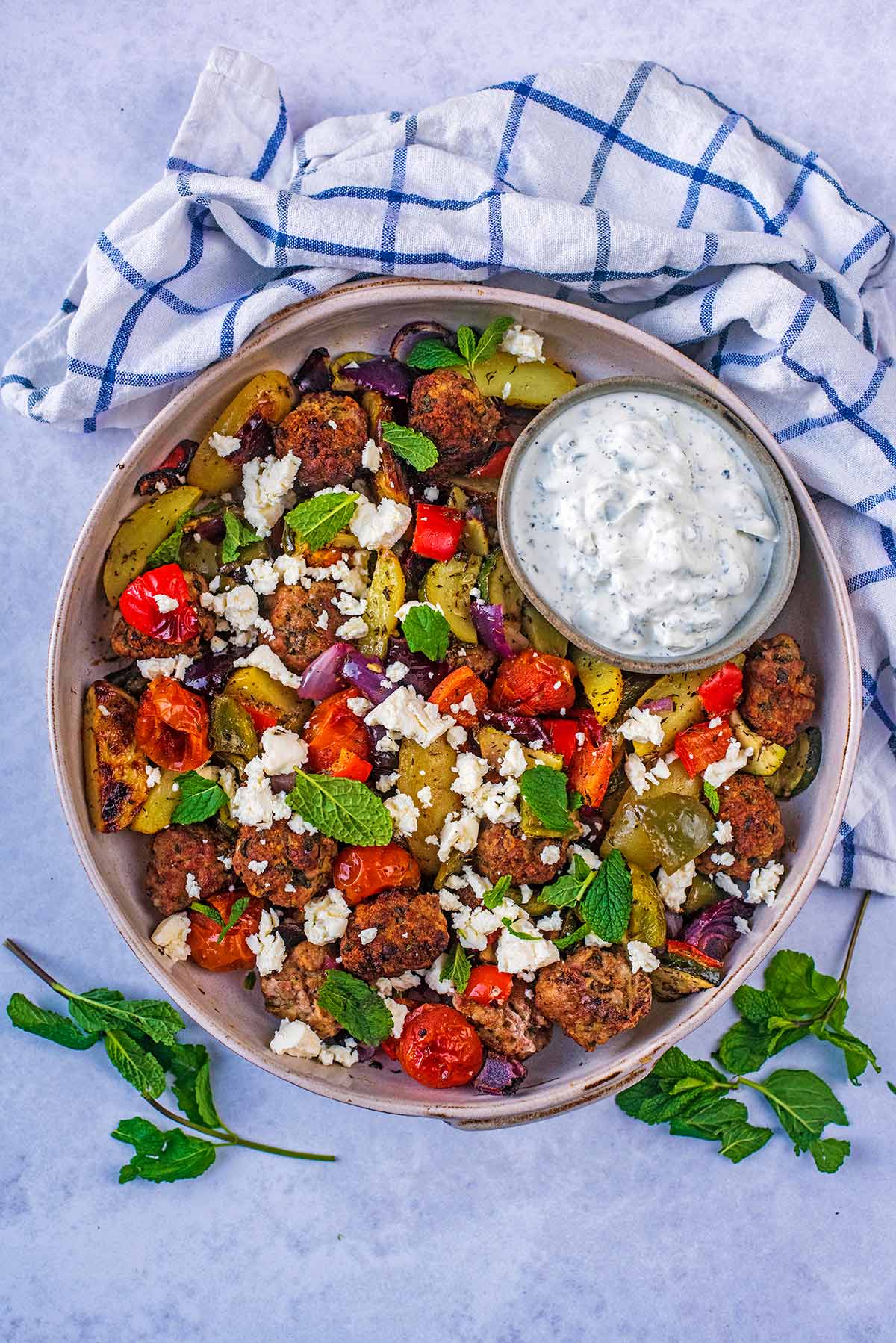 A large serving bowl containing meatballs, cooked vegetables and a small bowl of tzatziki.