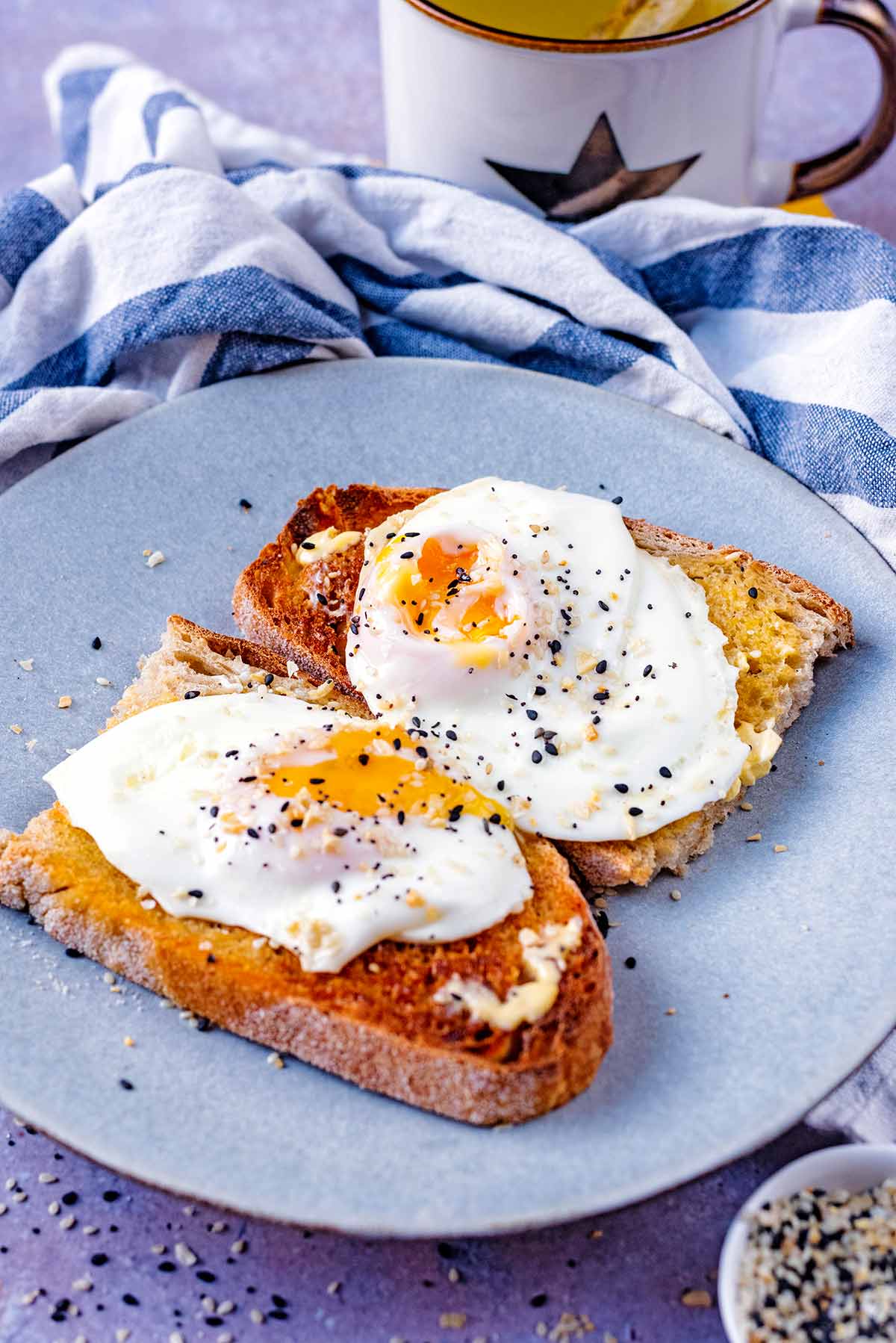 Two fried eggs on toast in front of a mug of tea.