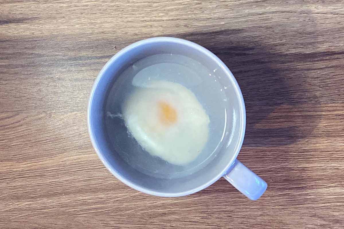 A mug containing water and a poached egg.